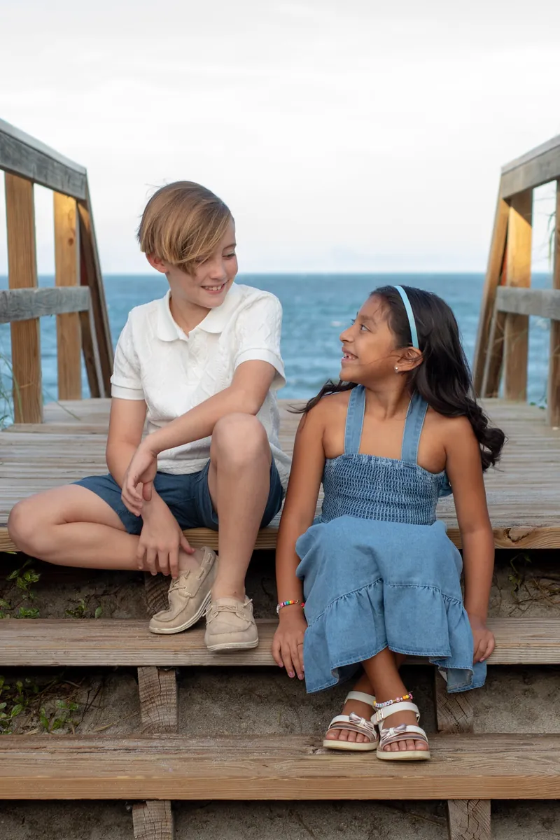 Brother and sister laughing together on wooden beach access steps in Jupiter, Florida
