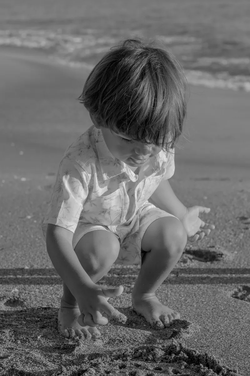 Black and white photo of a little boy playing in the sand at the water's edge